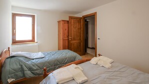 Een slaapkamer met twee bedden, een raam, een kledingkast en een open deur naar een andere kamer.