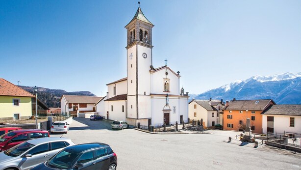 Església amb un campanar, envoltada d'edificis residencials i cotxes aparcats.