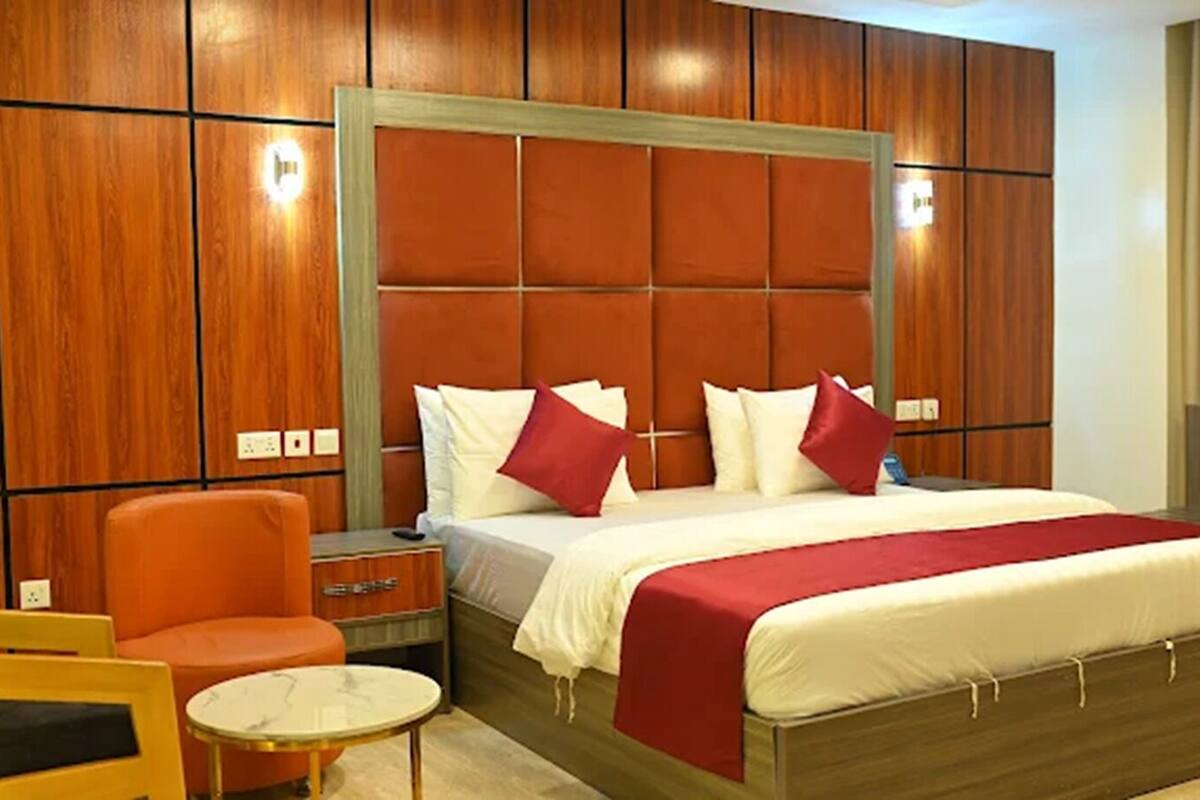 Une chambre d’hôtel avec un grand lit, une tête de lit en bois, un fauteuil orange, une petite table ronde et une table de chevet.