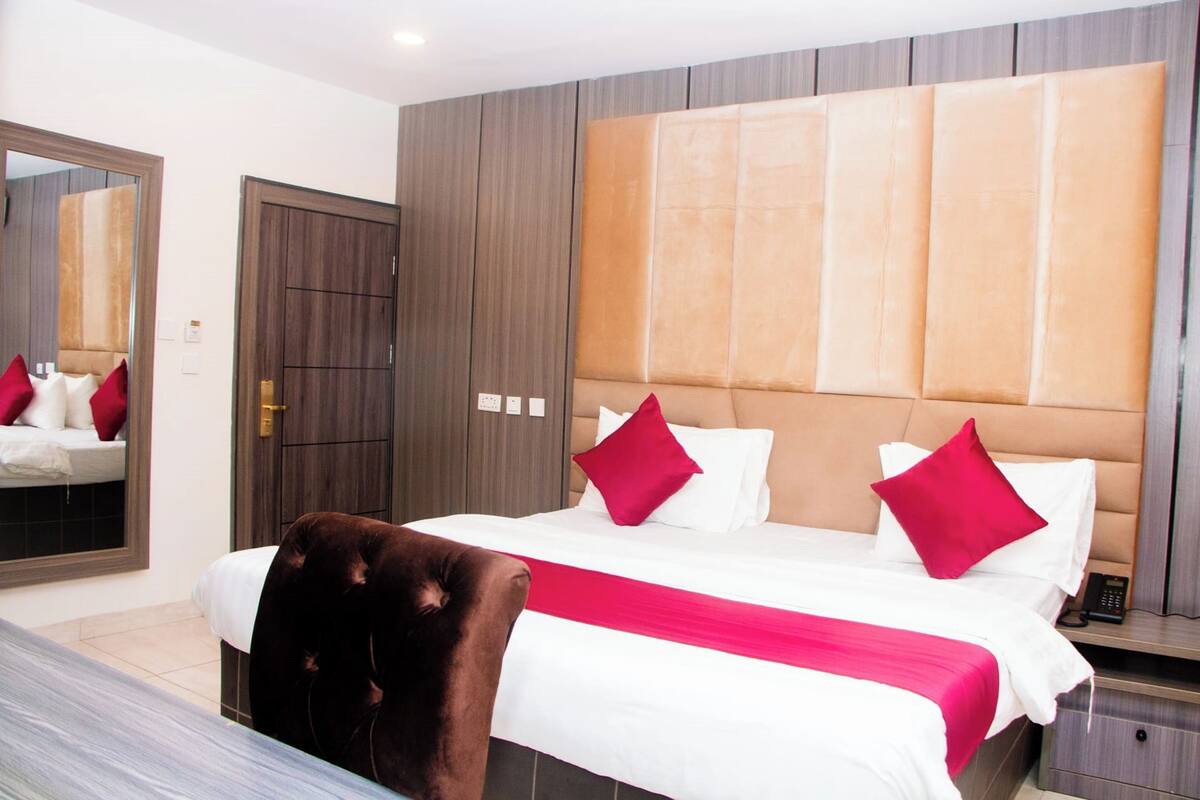 Une chambre d’hôtel avec un grand lit, une armoire en bois, un miroir et une table de chevet avec un téléphone.