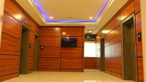 Eine moderne Liftlobby mit Holzwandverkleidung, einem digitalen Display und einer Decke mit eingelassener Beleuchtung.