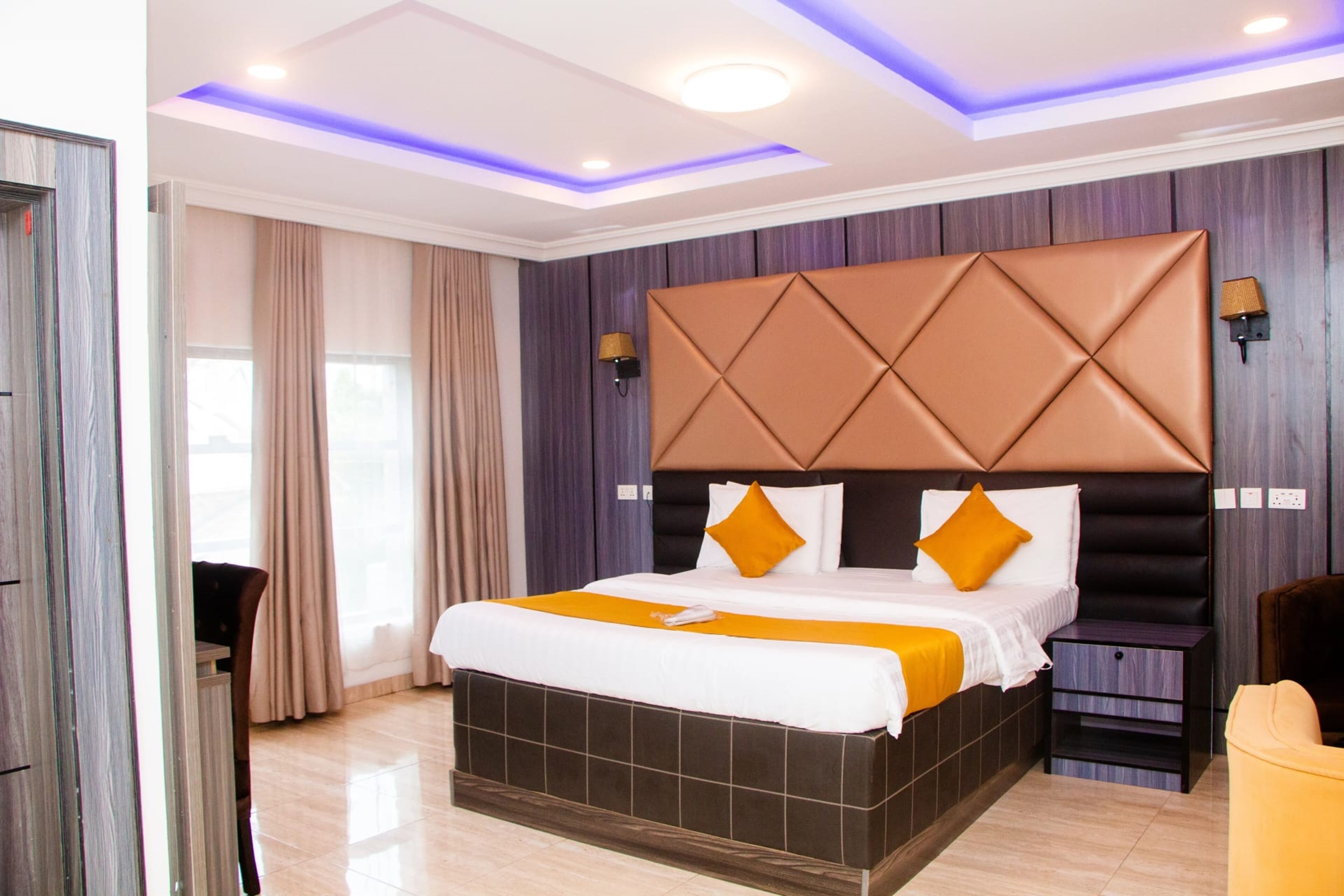Una habitación de hotel moderna con una cama grande, una mesita de noche, una silla y vistas al exterior.