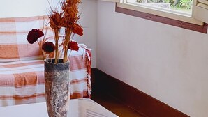 A cat standing on a concrete floor next to a wooden table with a vase of dried flowers. - Camping Tiradentes (Tiradentes)