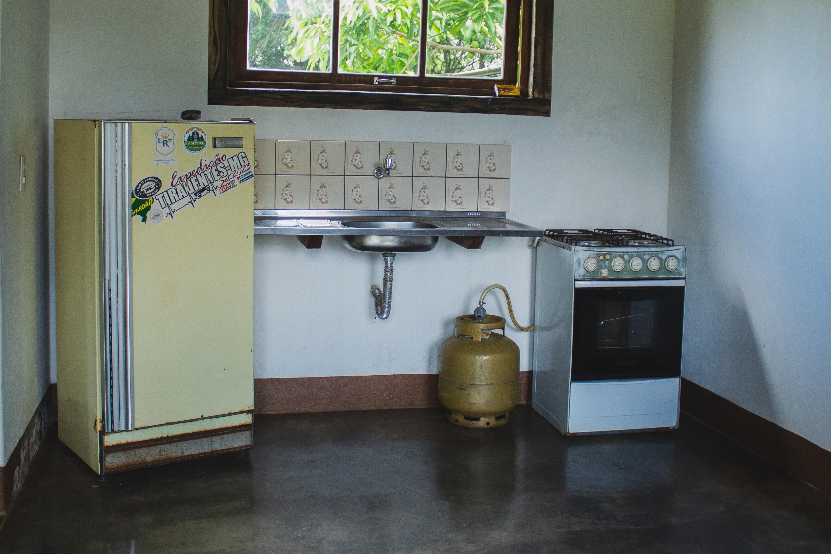 A compact kitchen with a refrigerator, sink, stove, and a gas cylinder.