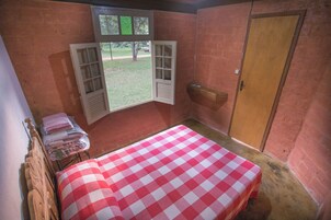Una habitación pequeña con una colcha a cuadros, una cama de madera, un ventanal con contraventanas y una puerta de madera.