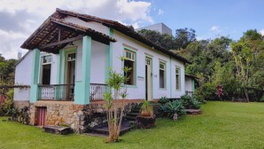 A two-story house with a stone foundation, green and white exterior, and a balcony with a metal railing. - Camping Tiradentes (Tiradentes)