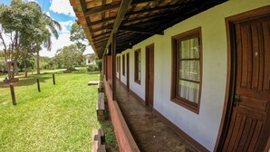 A corridor with wooden doors and windows, leading to a covered outdoor area with a grassy lawn and trees. - Camping Tiradentes (Tiradentes)