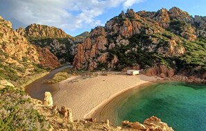 A coastal landscape with a sandy beach, a clear blue sea, and rocky cliffs.