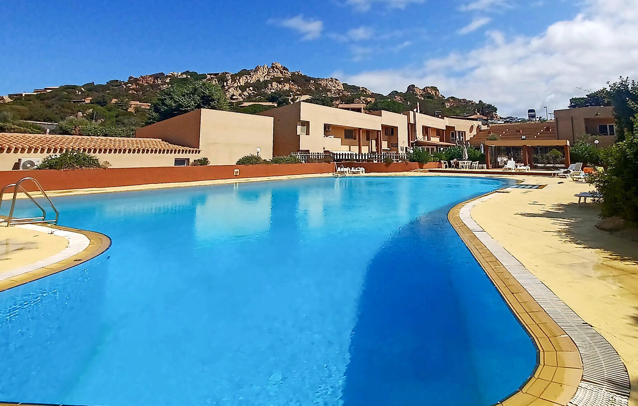 A swimming pool with a clear blue water, surrounded by a sandy beach and lounge chairs.