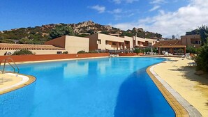 A swimming pool with a clear blue water, surrounded by a sandy beach and lounge chairs. - Lovely apartment in Costa Paradiso with swimming pool (Costa Paradiso)