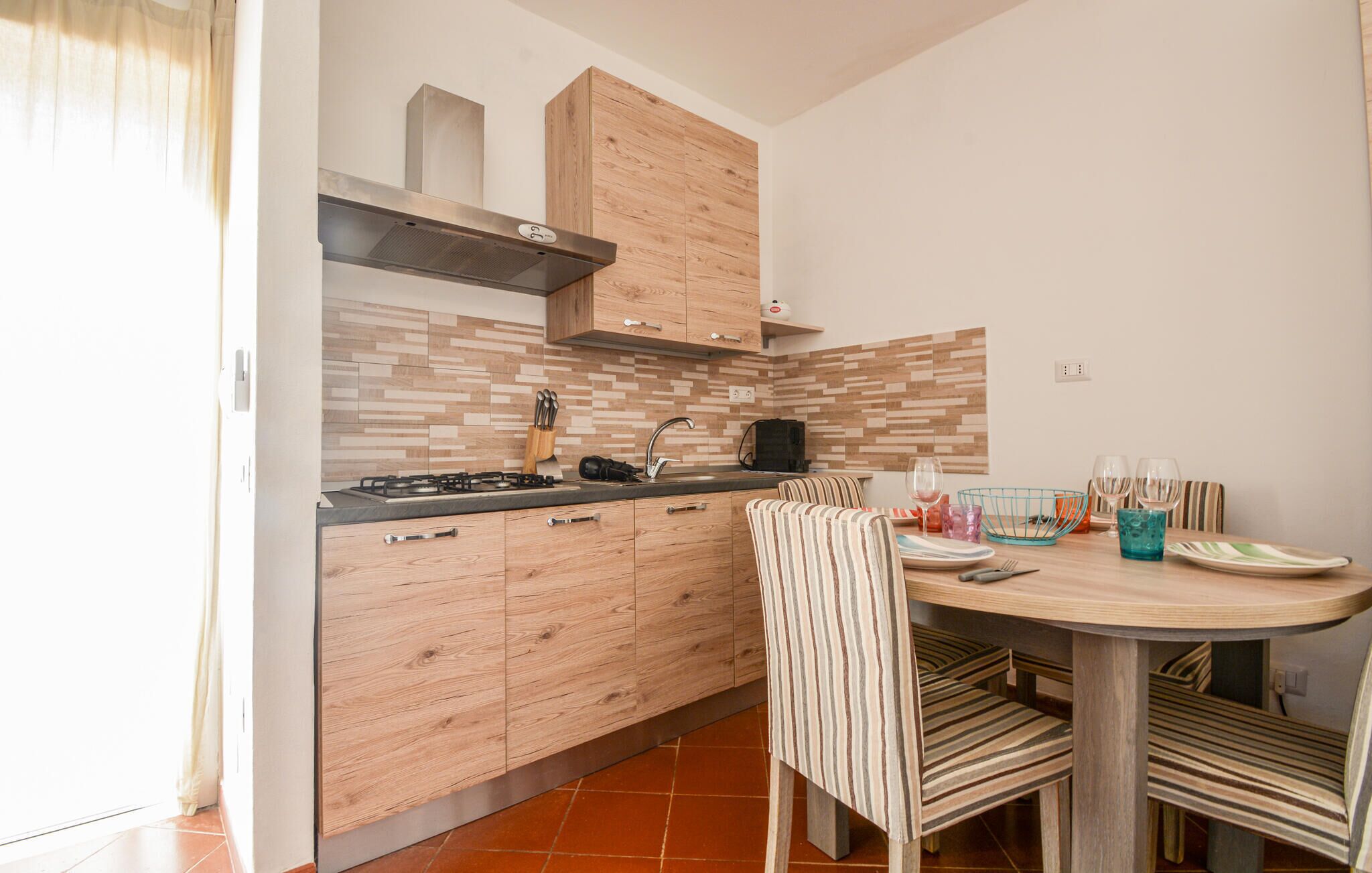 Una cocina moderna con armarios de madera, una estufa a gas y un comedor con sillas a rayas y una mesa redonda.