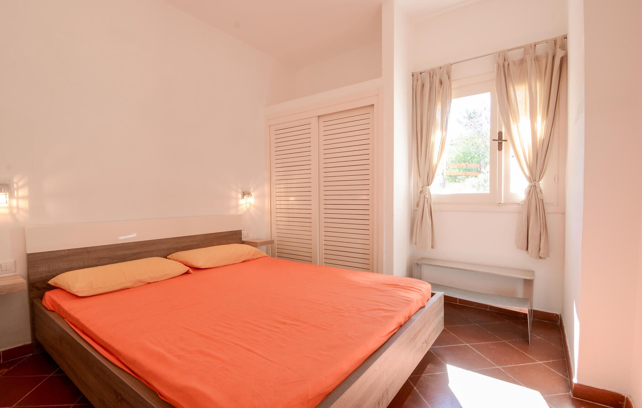 Un dormitorio con cama, mesita de noche, ventana con cortinas y armario.