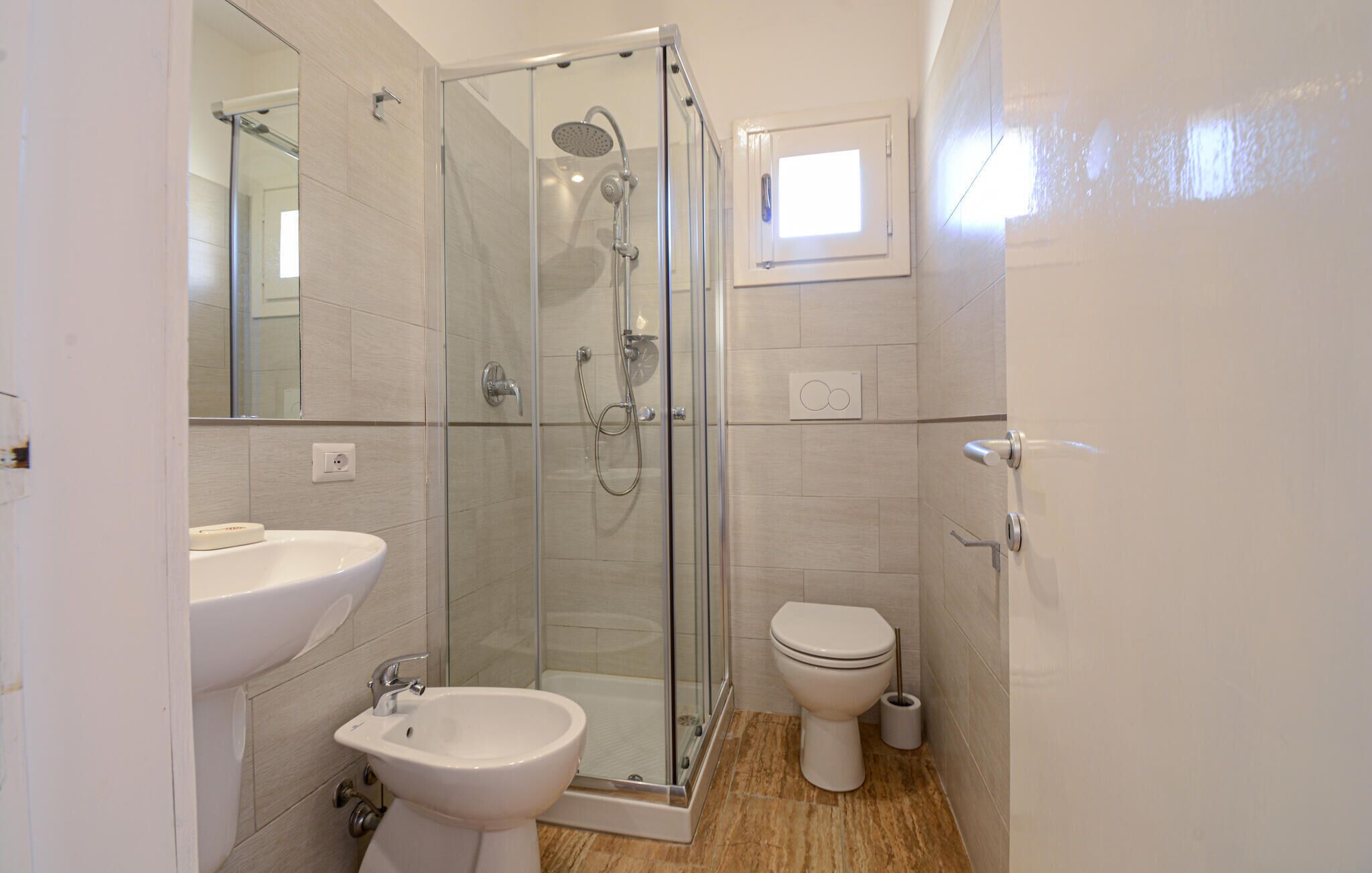 Et moderne badeværelse med et glasafskærmet brusebad, et pedestal håndvask og et toilet.