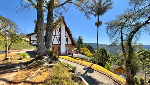 A traditional chalet with a sloped roof, surrounded by trees and a clear view of the valley. - Hortelã Village (Campos do Jordão)