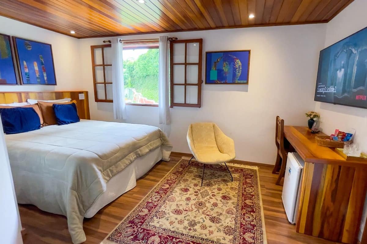 A bedroom with a bed, a chair, a desk with a computer, and artwork on the walls.