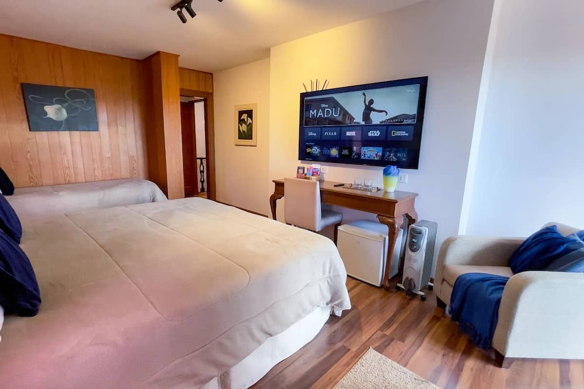 A hotel room with a large bed, a desk with a computer, a TV displaying movie options, and a small seating area.