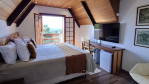 A bedroom with a bed, a desk, a TV, and a balcony with a view. - Hortelã Village (Campos do Jordão)