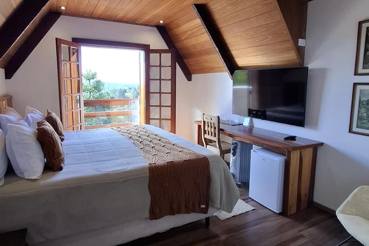 A bedroom with a bed, a desk, a TV, and a balcony with a view.