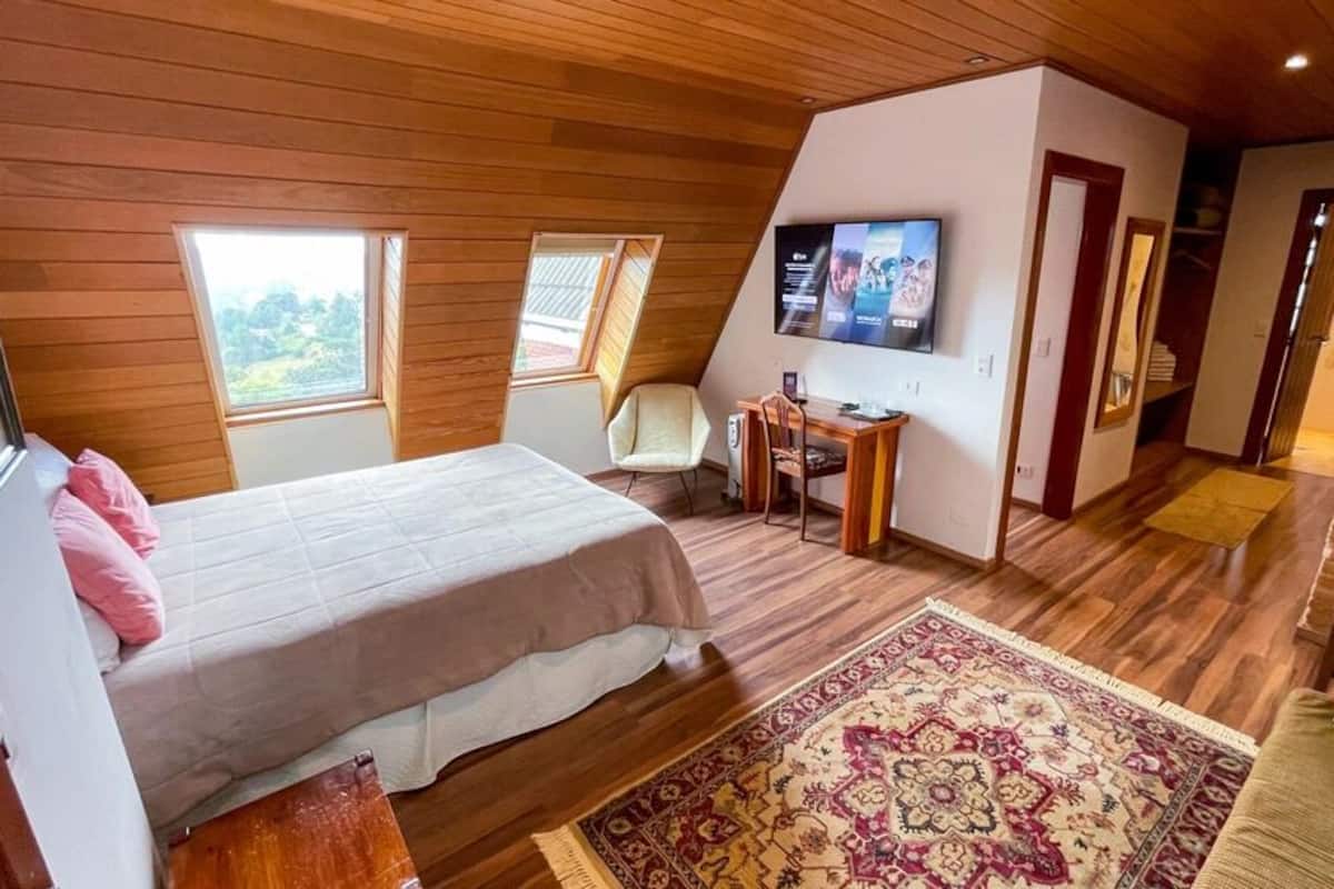 A bedroom with a bed, a desk, a TV, and a window.