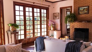 A living room with a sofa, a fireplace, a large window, and a door leading outside. - Hortelã Village (Campos do Jordão)