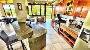 A modern kitchen with a dining area, large windows, and a view of greenery. - Villa Grande – Spacious 5-Bedroom Retreat with Private Pool in Manuel Antonio (Quepos)