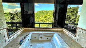 A bathroom with a large bathtub, a shower, and a toilet. It has a view of a lush green landscape through large windows. - Villa Grande – Spacious 5-Bedroom Retreat with Private Pool in Manuel Antonio (Quepos)