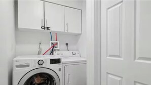 Una sala de lavandería con lavadora y secadora de carga frontal, alacenas blancas en la parte superior y tomas de corriente visibles.
