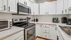 Una cocina moderna con armarios blancos, microondas, estufa, tostadora y cafetera.