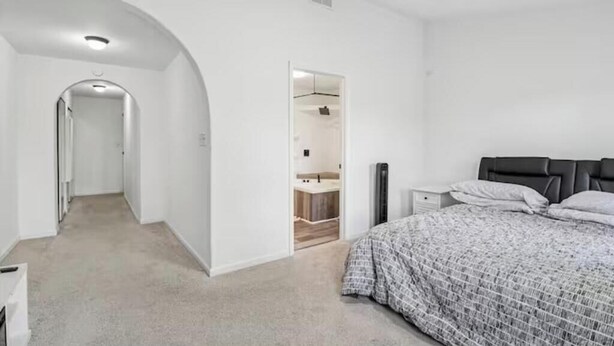 Un dormitorio con cama, mesita de noche, armario y un pasillo que lleva a un baño.
