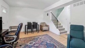Amplia sala de estar con escalera, mesa de comedor con sillas, sofá y alfombra estampada.