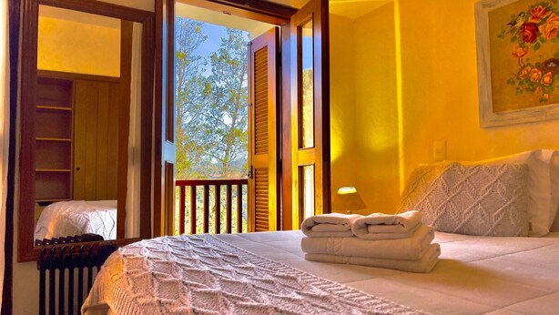 A bedroom with a bed, a window with a view of trees, and a painting on the wall. - Pousada Hortelã (Campos do Jordão)