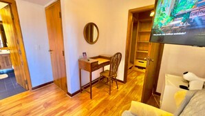A room with a wooden floor, a desk with a chair, a round mirror, and a television displaying a nature scene. - Pousada Hortelã (Campos do Jordão)