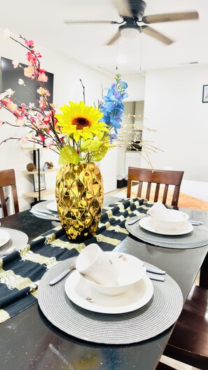 A dining table with a golden vase of flowers, white plates, and a black tablecloth. - Modern & Cozy Summerville Apt - Fully Equipped (Summerville)