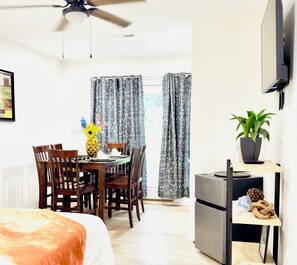 A hotel room with a bed, a dining table with chairs, a ceiling fan, a TV mounted on the wall, and a potted plant. - Modern & Cozy Summerville Apt - Fully Equipped (Summerville)