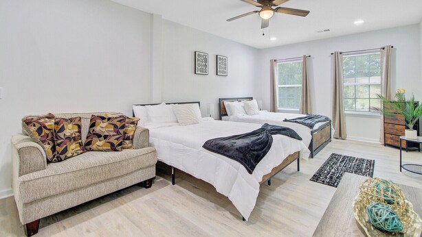 A bedroom with two beds, a sofa, a ceiling fan, and large windows.