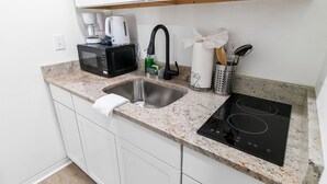 A compact kitchen with a sink, a microwave, a kettle, a coffee maker, and a stovetop.