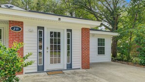 A single-story house with a brick facade, numbered 211, featuring a front door, a garage door, and a small porch area.