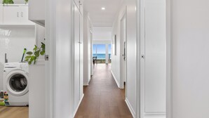 Un couloir propre et blanc, avec un lave-linge sur le côté gauche, qui mène à un balcon offrant une vue sur la mer.
