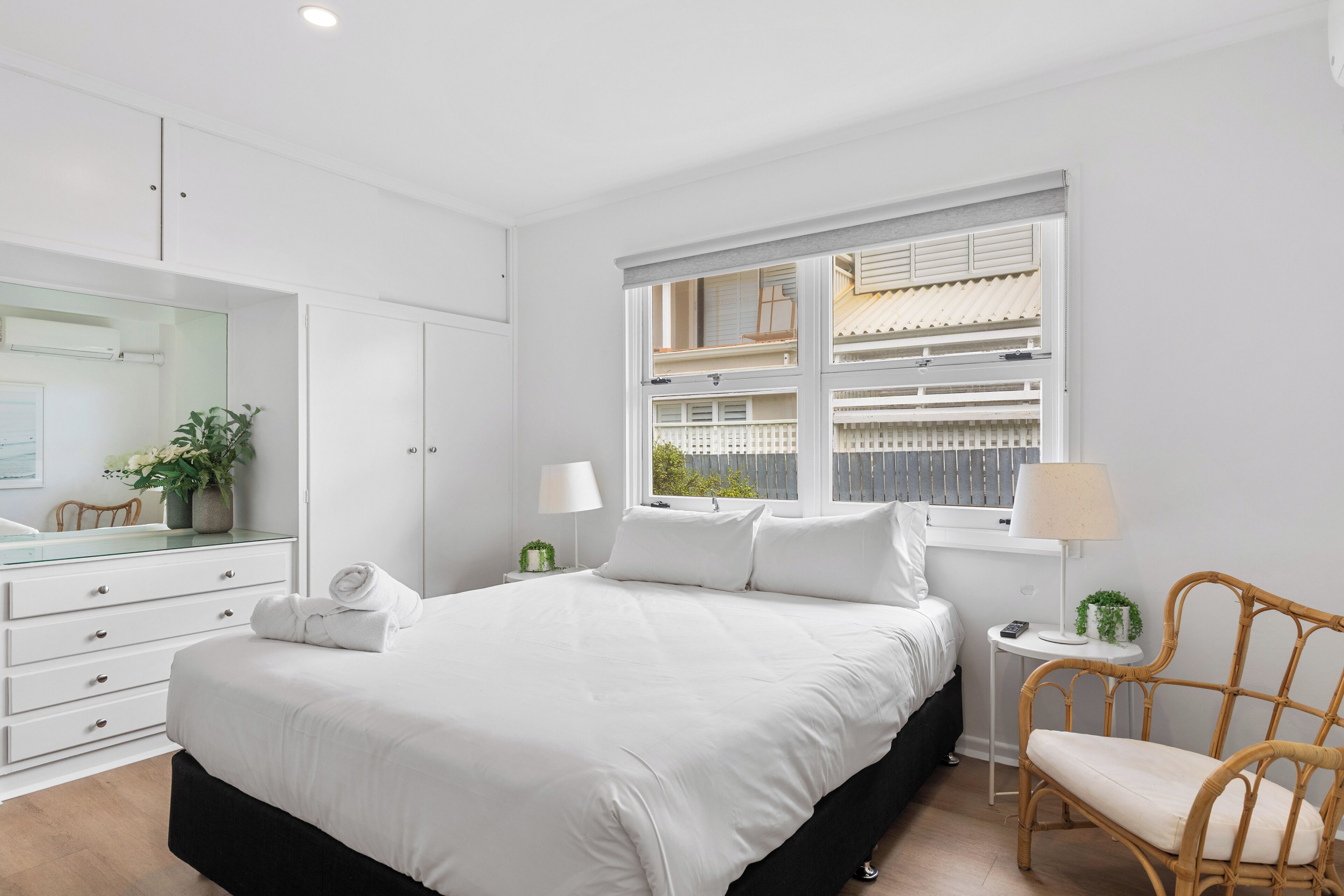 A bedroom with a large bed, a dresser, a chair, a window with a view, and a bedside table with a lamp.