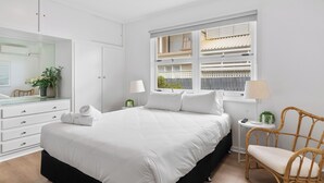 Une chambre à coucher avec un grand lit, une commode, une chaise, une fenêtre donnant sur un beau paysage et une table de chevet avec une lampe.