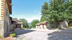 A cobblestone street with rustic stone buildings, a large tree, and a clear sky.