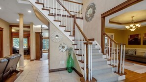 Un vestíbulo espacioso con una imponente escalera, un comedor y una sala de estar con sofá y candelabro.