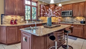 A spacious kitchen with wooden cabinets, a granite countertop, a large island with bar stools, and a decorative vase with flowers.