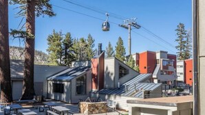 A modern building with a sloped roof, outdoor seating area, and a cable car in the background. - Canyon View at Canyon Lodge (Mammoth Lakes)