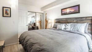 A bedroom with a large bed, a wooden headboard, a nightstand, a lamp, and a framed picture on the wall. - Canyon View at Canyon Lodge (Mammoth Lakes)