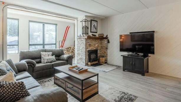 A modern living room with a stone fireplace, a grey sofa, a coffee table, and a TV on a stand. - Canyon View at Canyon Lodge (Mammoth Lakes)