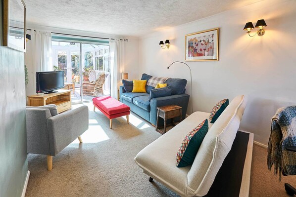 A living room with a sofa, a red ottoman, a television, and a small table. - Host Stay Bodiam Close (Seaford)