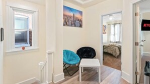 Un apartamento moderno con una pintura de paisaje urbano, una pequeña mesa blanca y una silla azul.