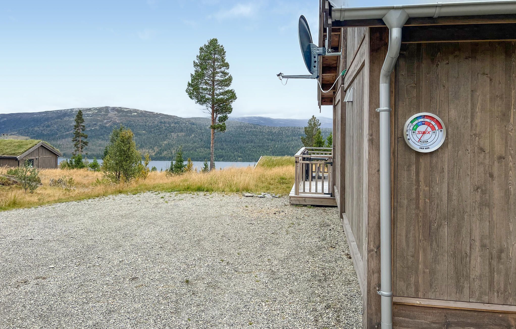 A wooden cabin with a gravel driveway, a satellite dish, and a view of a lake and mountains.