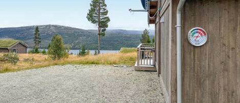 A wooden cabin with a gravel driveway, a satellite dish, and a view of a lake and mountains.